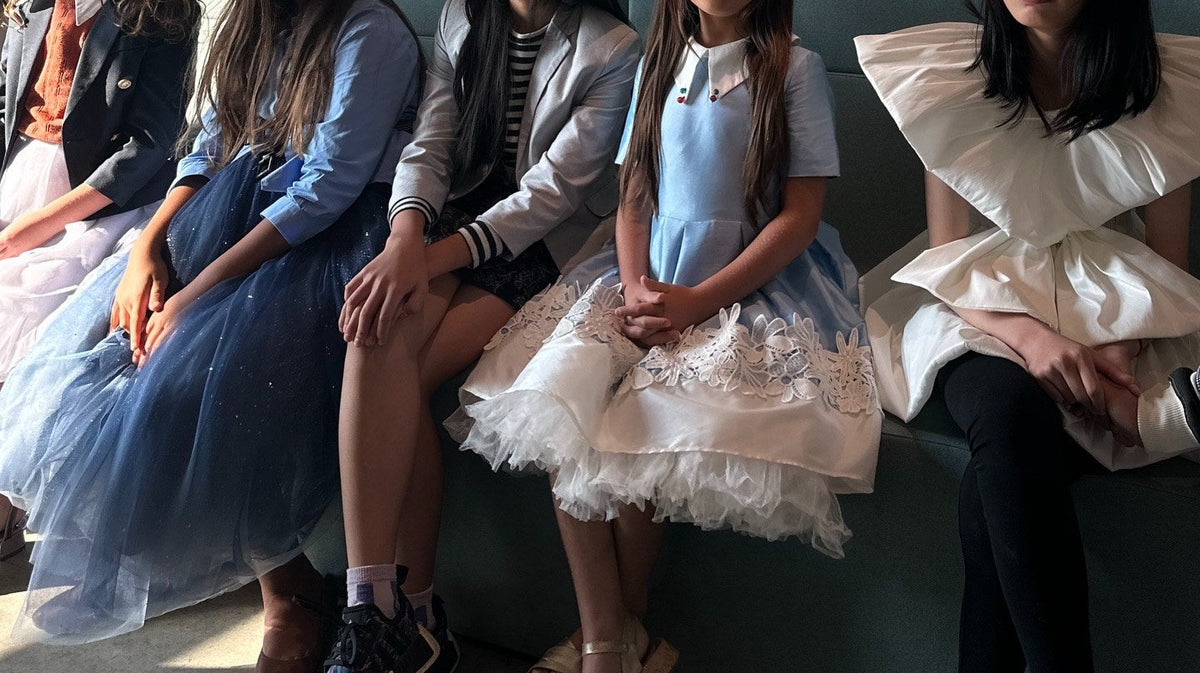 Backstage at Vancouver Kids Fashion Week 2026: five girls in blazers, big collars, tulle and a sculptural white bow dress